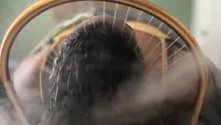 Woman with dark curly hair rleaxing under the head spa halo with water spraying on her head.